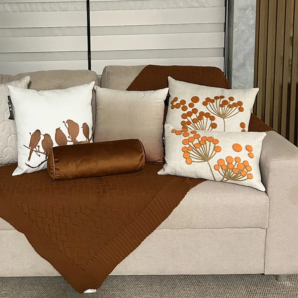 Sofá com almofadas estampadas em laranja e manta de tricô marrom